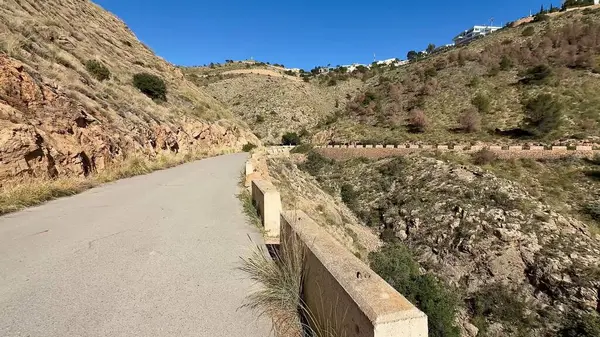 Canlı yeşillik ve heybetli kayalık araziyle çerçevelenmiş dolambaçlı bir dağ yolunun nefes kesici manzarası.