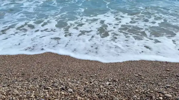 Yumuşak dalgalar hoş, çakıllı bir plaja hafifçe çarpıyor, güzel ve sakin bir sahil atmosferi yaratıyor.