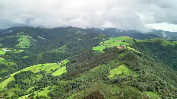 Dramatik bulutlu bir gökyüzünün altında canlı yeşil tepeleri gösteren nefes kesici bir manzara.