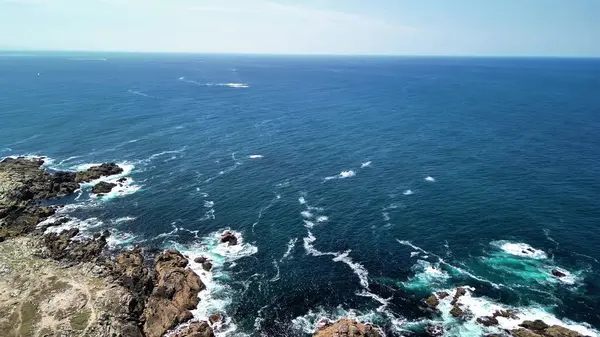 Okyanus dalgalarının açık mavi bir gökyüzü altında kayalık kıyılara çarptığı nefes kesici hava görüntüleri..