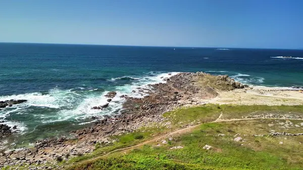 Kayalık bir kıyı şeridinin ve güzel okyanusun güneşli gününde dalgaların tadını çıkar.