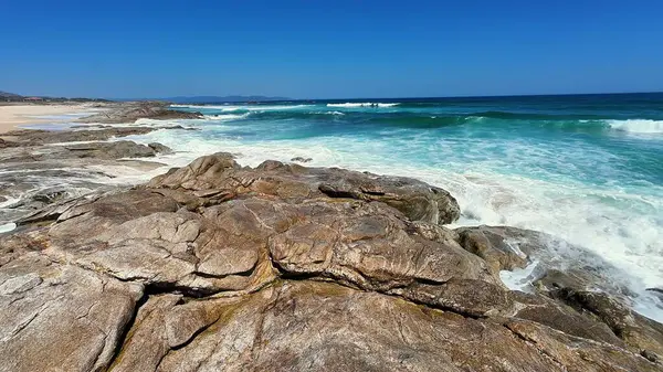 Göz kamaştırıcı bir kayalık kıyı şeridi açık ve güneşli gökyüzünün altında canlı mavi okyanusla karşılaşıyor.