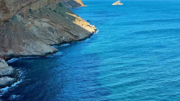 Engebeli kayalıkların sersemletici hava görüntüleri sakin gök mavisi sularla buluşuyor. Resimli bir kıyı manzarası yaratıyor..