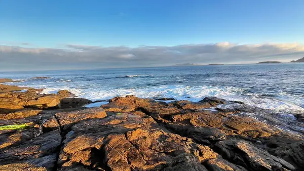 Muhteşem okyanus dalgalarının berrak bir gökyüzünün altında kayalık kıyılara çarpmasının çarpıcı ve resimsel bir görüntüsü.
