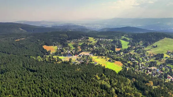 Havadan çekilen bir fotoğraf, dingin bir köyün yanında canlı yeşil bir orman yakalıyor, çarpıcı güzellikler sergiliyor.