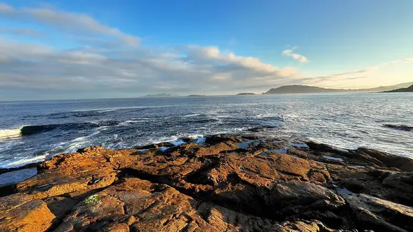 Engin okyanusla canlı bir gökyüzünün altında zarif bir şekilde buluşan kayalık kıyı şeridinin nefes kesici bir görüntüsü.