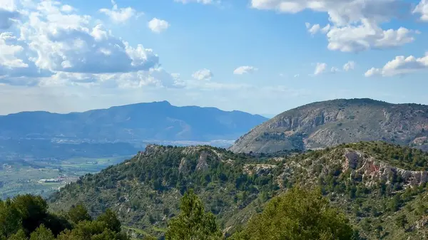 Pofuduk beyaz bulutlarla dolu canlı mavi gökyüzüne bakan görkemli dağların nefes kesici manzarası.