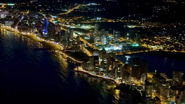 Kıyı kenti kıyı şeridi boyunca renkli ışıklarla parıldayan nefes kesici gece hava manzarası.