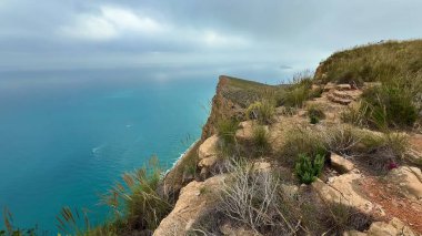 Şaşırtıcı güzellikteki manzara bulutlu gökyüzünün altında dalgalı mavi bir okyanusla engebeli bir uçurum kenarı sergiliyor.