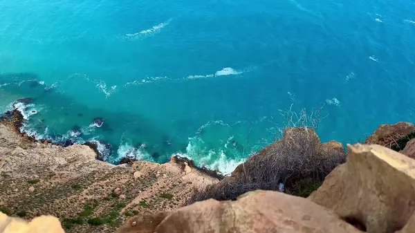 Çarpıcı hava manzarası, huzurlu bir sahil şeridi boyunca kayalıklarla harmanlanmış turkuaz bir deniz gösteriyor.