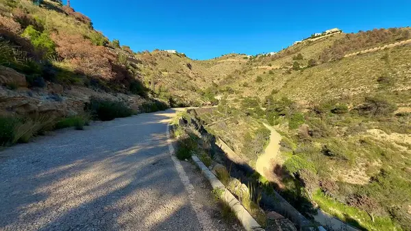 Sakin, sakin, çakıllı bir yolda, nefes kesici dağ manzarası ve açık mavi bir gökyüzü sunan bir yürüyüş yapın.