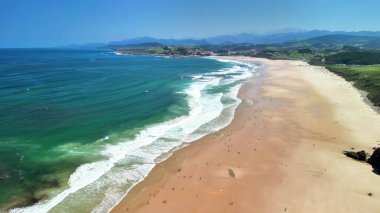 Yumuşak dalgalar ve berrak mavi gökyüzü ile nefes kesici bir sahil manzarası, rahatlama ve keyif için mükemmel.