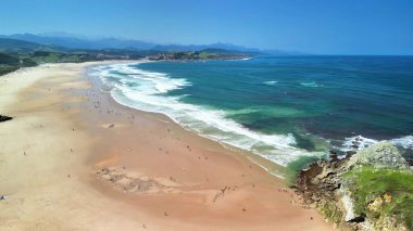 Bu hava manzarası, dingin bir sahilin güzelliğini yakalar. Altın kumlarını ve canlı okyanus dalgalarını gözler önüne serer.