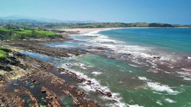 Kayalık kıyı şeridinin sakin manzarası berrak suları ve parlak mavi gökyüzünün altında yemyeşil tepeleri barındırır.