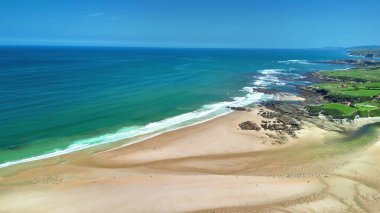 Çevresinde turkuaz suları ve yemyeşil tepeleri olan sakin bir plajın çarpıcı hava manzarasını tecrübe edin.