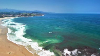 Bu büyüleyici hava fotoğrafı, dalgaların berrak mavi sularla buluştuğu çarpıcı ve sakin bir sahili gösteriyor.