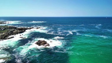 Nefes kesici hava görüntüleri, okyanus dalgalarının canlı renk ve hareketle kayalara çarpmasının güzelliğini yakalar.