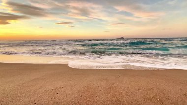 Güzel, sakin bir sahil sahnesi büyüleyici bir günbatımını yakalıyor okyanusun yumuşak dalgalarıyla birlikte.