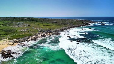 Hava manzarası, berrak turkuaz suları ve yemyeşil bitki örtüsüyle dramatik bir kıyı şeridi gösteriyor.