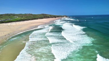 Güzel bir kumsal, nazik dalgalar ve suyun tadını çıkaran sörfçülerle nefes kesici bir hava çekimi..