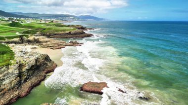 Sahilde dalgalar, engebeli kayalar ve yemyeşil manzaralarla güzel kıyı manzarasının tadını çıkarıyorum.
