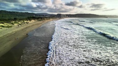 Büyüleyici bir sahil sahnesi güzel dalgalar ve günbatımında geniş bir kıyı manzarası sergiliyor.