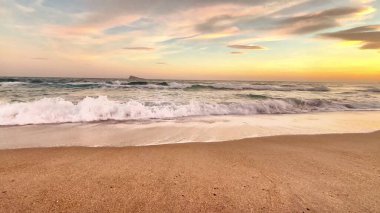 Gün batımında yumuşak dalgaları yakalayan sakin bir sahil sahnesi, rahatlama ve doğa temaları için ideal.