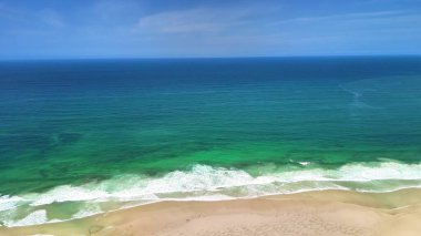 Parlak turkuaz okyanusun ve açık mavi gökyüzünün altındaki altın plajın nefes kesici hava manzarasının tadını çıkarın.