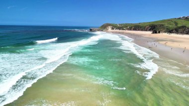 Sersemletici bir hava görüntüsü, berrak turkuaz su ve canlı yeşillik içeren pitoresk bir sahili gösteriyor..