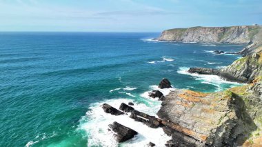 Bu hava manzarası, heybetli uçurumlara çarpan canlı mavi dalgalarla nefes kesici bir kayalık kıyı şeridi yakalıyor.