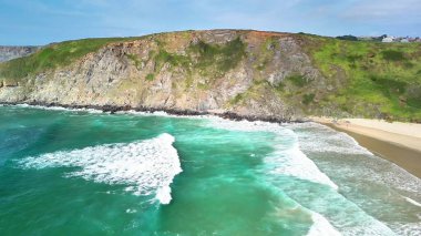 Turkuaz okyanus dalgalarının kayalık kayalıklara çarptığını gösteren çarpıcı hava manzarasına tanık olun.