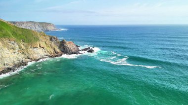 Berrak turkuaz okyanus dalgalarıyla buluşan engebeli kayalıkların nefes kesici ve çarpıcı hava manzaraları.