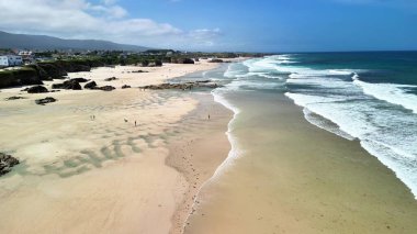 Göz kamaştırıcı bir hava görüntüsü. Huzurlu, güzel bir sahili, dalgalı ve kayalık bir kıyı şeridini gösteriyor.