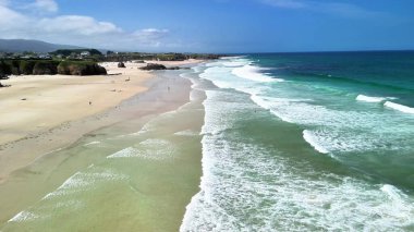 Bu nefes kesici dron görüntüsü güneşli bir günde sakin dalgaları yavaşça kumlu kumsalda yakalar.