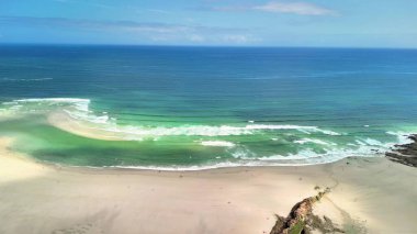 Nefes kesici bir hava manzarası sakin bir plajı, nazik dalgaları ve büyüleyici mavi okyanusu gösteriyor.