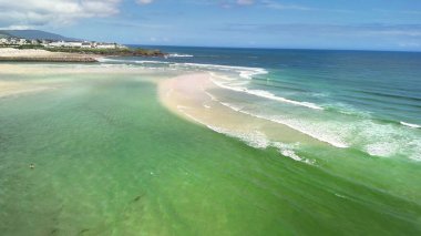 Nefes kesici bir hava fotoğrafı berrak suları ve sakin dalgaları olan sakin bir sahili gösteriyor.