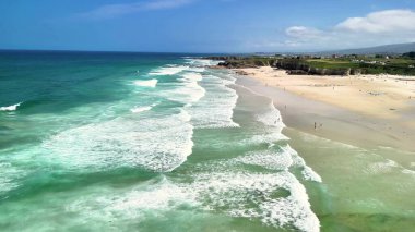 Nefes kesen kıyı manzarası turkuvaz suları ve altın kumları sergiliyor, hepsi berrak mavi bir gökyüzünün altında