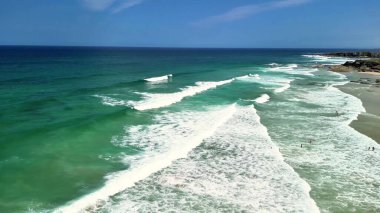 Sakin okyanus dalgalarının ve berrak mavi gökyüzünün altındaki canlı turkuaz suların nefes kesici hava manzarasının tadını çıkar.