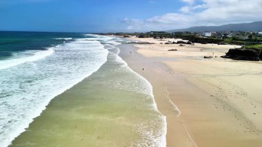 Sakin bir sahil manzarası yaşayın. Nazik dalgalar, yumuşak altın kum ve berrak mavi gökyüzü.