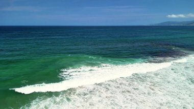 Hava görüntülerinde muhteşem turkuaz sular ve sakin dalgalar sergileniyor. Resimli kumlu bir plajda yavaşça yuvarlanıyorlar.