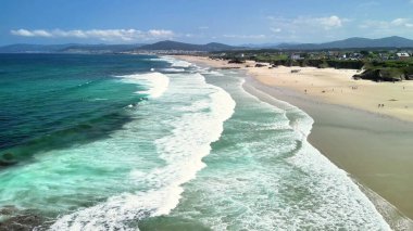 Zarif dalgaların ve açık mavi gökyüzünün bulunduğu nefes kesici ve resimli bir sahilin havadan görünüşü.