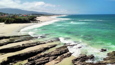 Canlı, gür yeşillik, dalgalı dalgalar ve sakin bir sahil şeridini barındıran nefes kesici sahil manzarası.