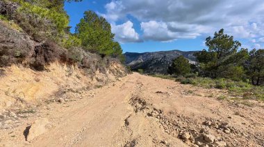 Engebeli, dolambaçlı bir toprak yol, temiz, mavi gökyüzü ile süslenmiş, görkemli dağlık bir arazide yılan gibi yol alır.