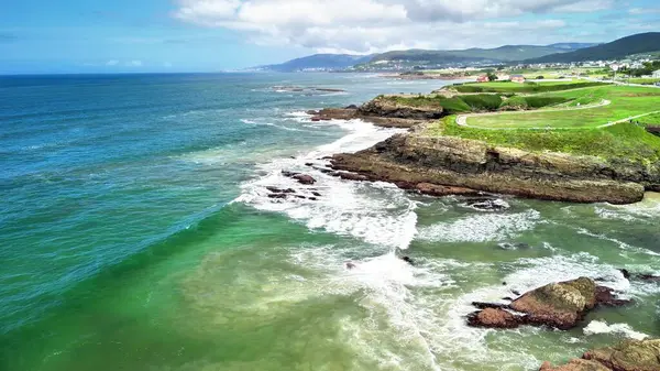 Çarpıcı bir hava manzarası dalgaların engebeli bir kıyıya çarptığını, canlı okyanus renklerini güzellikle renklendirdiğini gösteriyor.