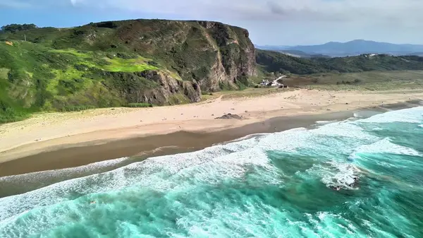 Huzurlu ve sakin bir plajın nefes kesici hava manzarası, canlı dalgalar ve yemyeşil uçurumlar.