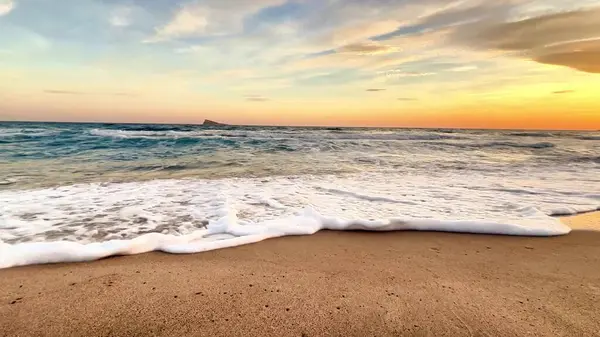 Nazik dalgaların sakin bir sahnesiyle baş döndürücü ve renkli bir günbatımında altın sahili hafifçe okşayarak