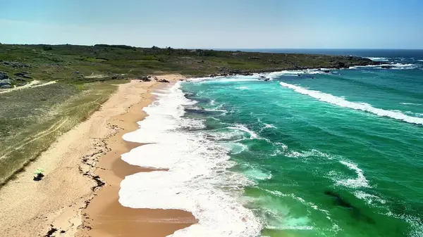 Canlı turkuaz suları ve yumuşak altın kumlarıyla nefes kesici güzel bir sahili gösteren bir hava manzarası.