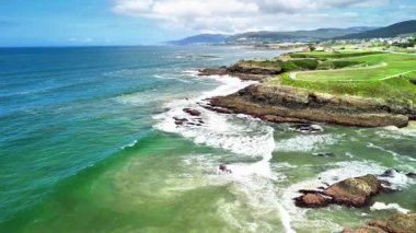 Çarpıcı bir hava manzarası dalgaların engebeli bir kıyıya çarptığını, canlı okyanus renklerini güzellikle renklendirdiğini gösteriyor.