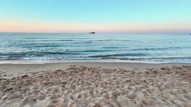 Huzurlu ve sakin bir sahil sahnesi. Alacakaranlıkta sakin bir gökyüzünün altında hafif dalgalar kıyıya vuruyor.