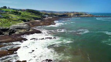 Çarpıcı sahil şeridinde kayalık kıyılara vuran dalgalar var, yemyeşil tepeler güzel bir zemin görevi görüyor.